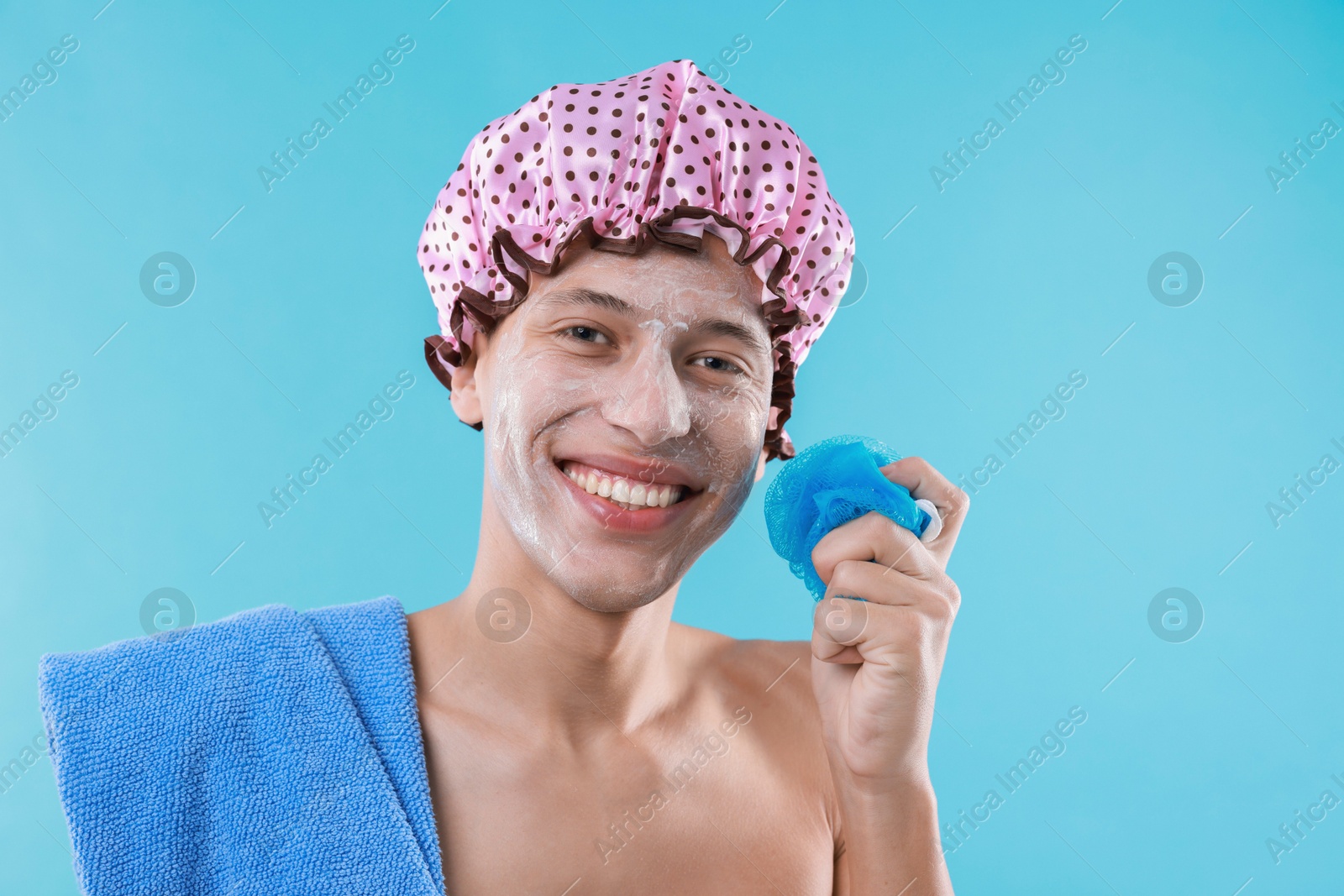 Photo of Man with shower cap, towel and mesh sponge on light blue background