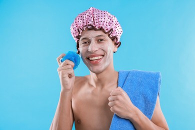 Photo of Man with shower cap, towel and mesh sponge on light blue background