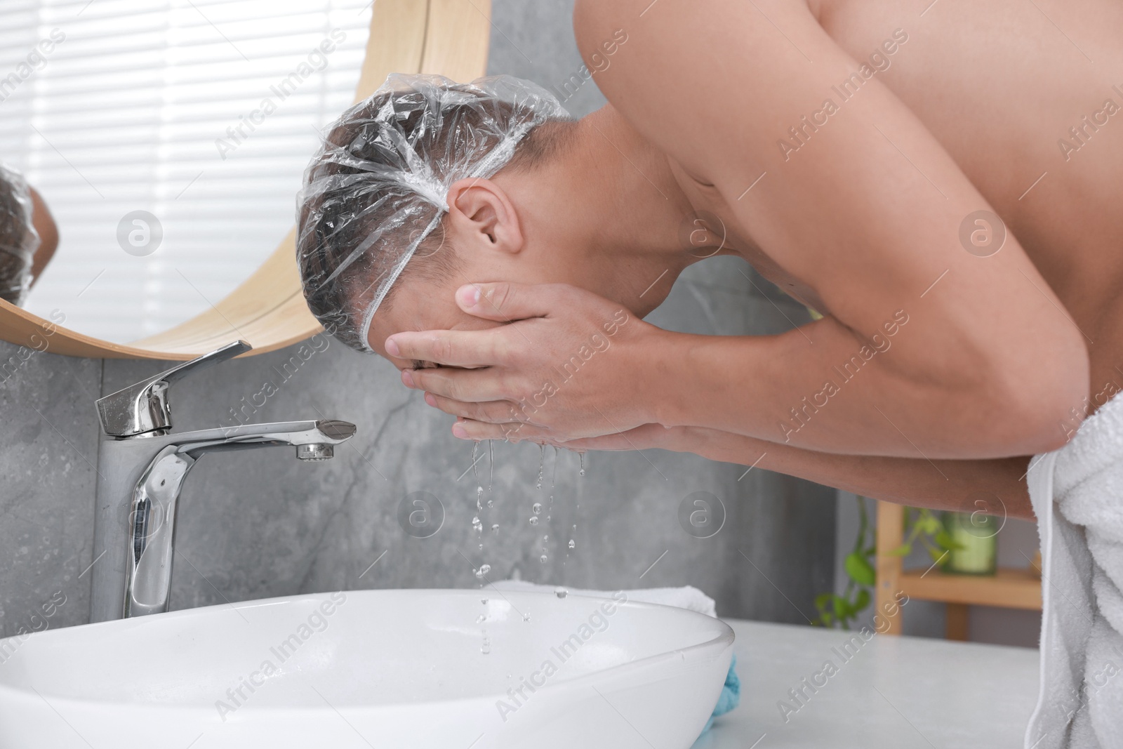 Photo of Man wearing shower cap washing his face in bathroom