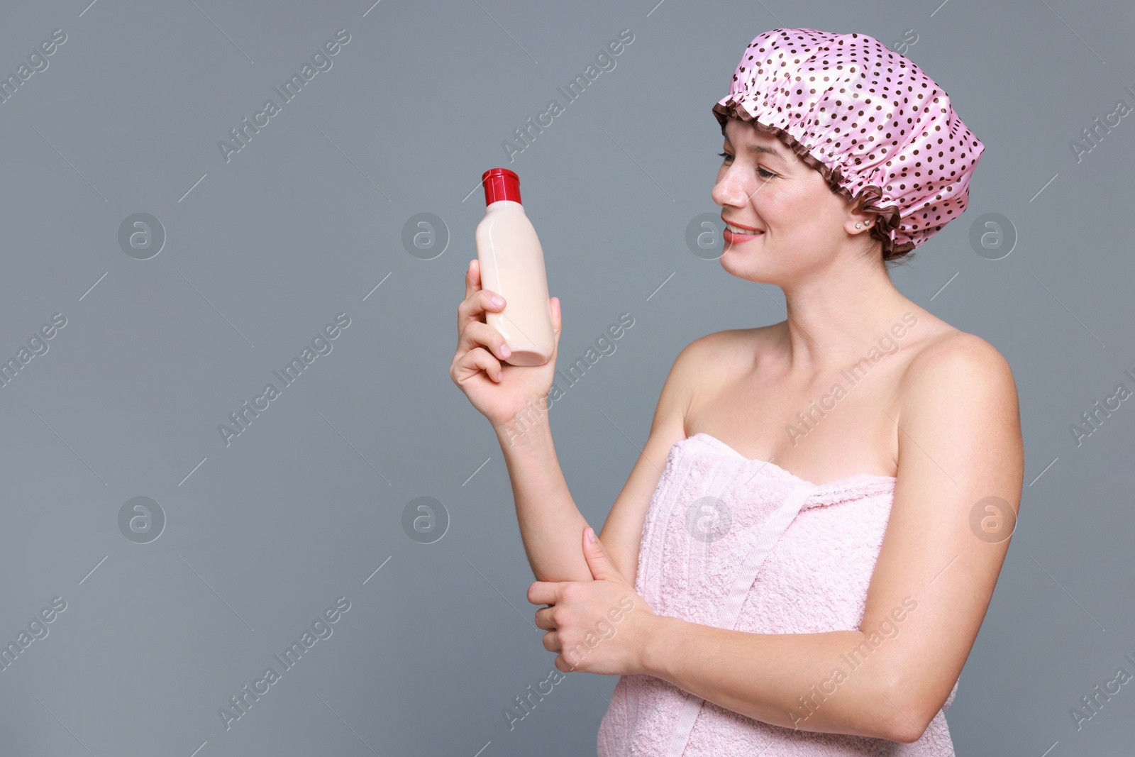 Photo of Woman with pink shower cap and shampoo on grey background, space for text