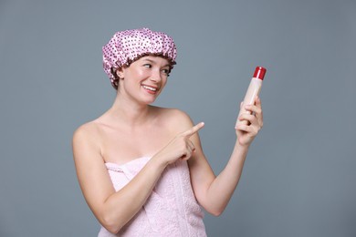 Photo of Woman with pink shower cap and shampoo on grey background