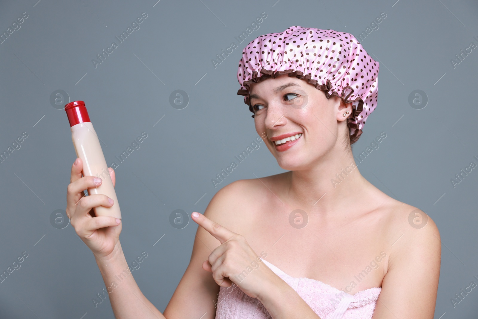 Photo of Woman with pink shower cap and shampoo on grey background