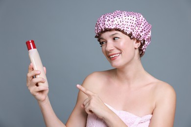 Photo of Woman with pink shower cap and shampoo on grey background