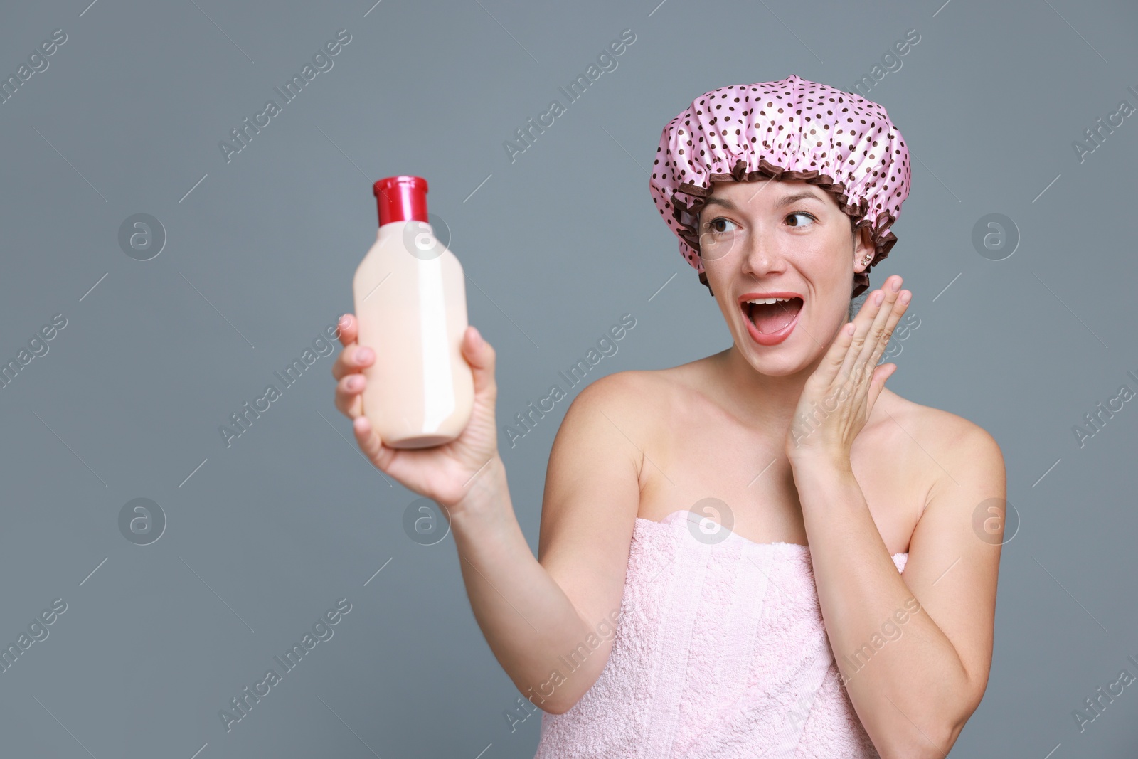 Photo of Woman with pink shower cap and shampoo on grey background, space for text