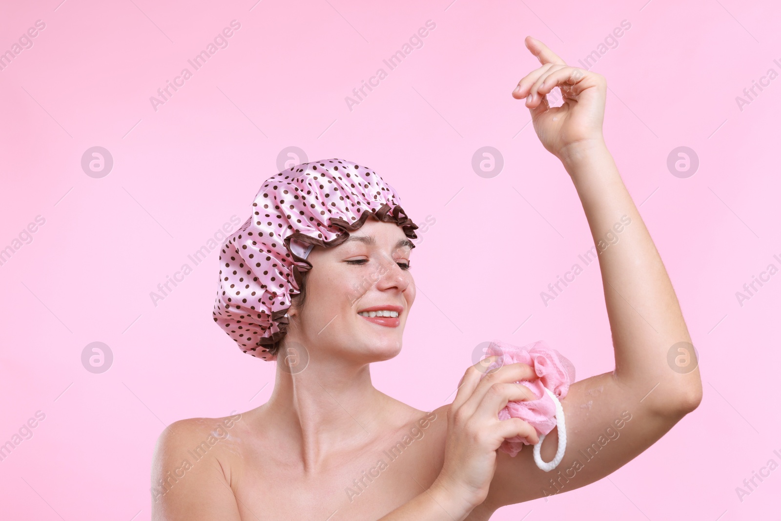 Photo of Woman with shower cap and mesh sponge on pink background