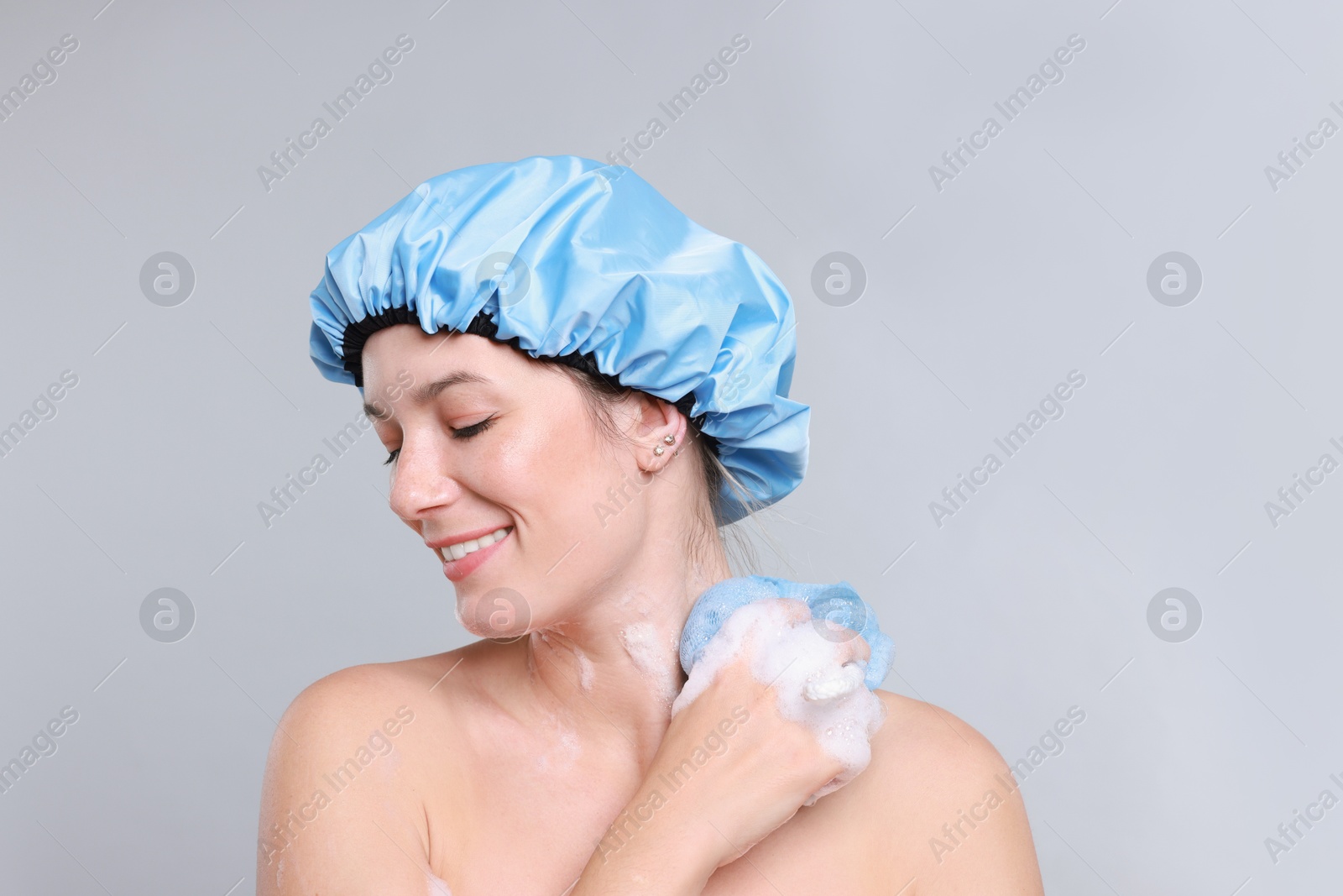 Photo of Woman with shower cap and mesh sponge on grey background