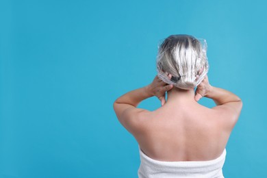 Photo of Woman wearing shower cap on light blue background, back view. Space for text