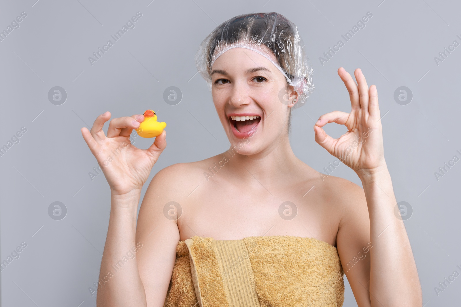 Photo of Woman with shower cap and bath duck showing ok gesture on grey background