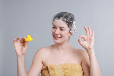 Photo of Woman with shower cap and bath duck showing ok gesture on grey background