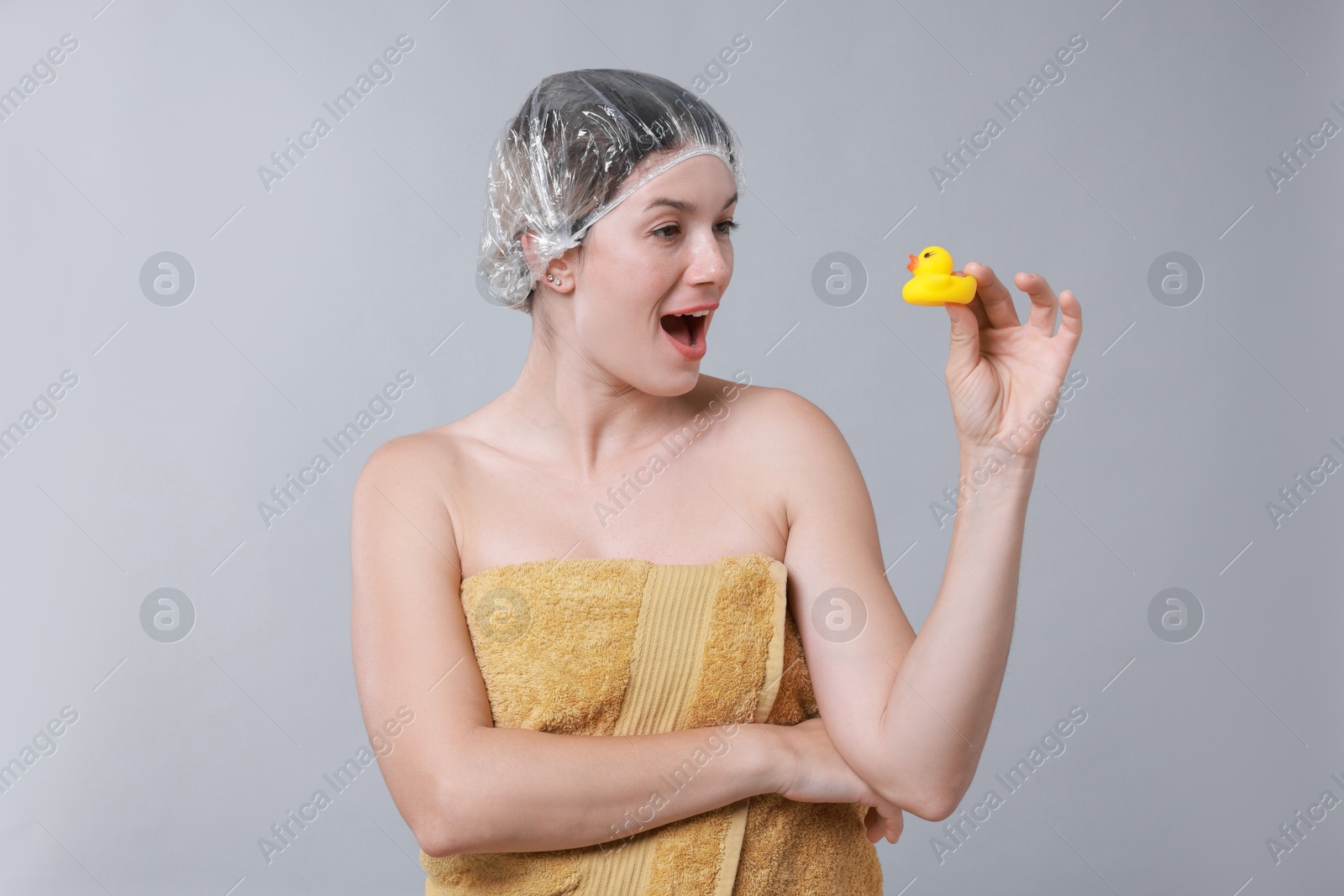 Photo of Woman with shower cap and bath duck on grey background