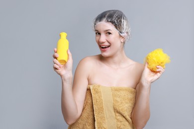 Photo of Woman with shower cap, shampoo and mesh sponge on grey background