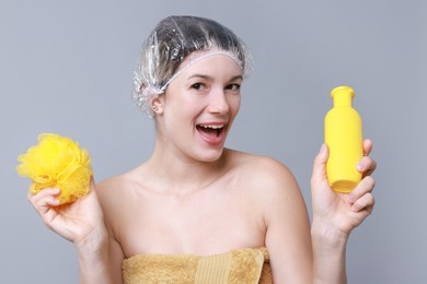 Photo of Woman with shower cap, shampoo and mesh sponge on grey background