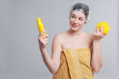 Photo of Woman with shower cap, shampoo and mesh sponge on grey background, space for text