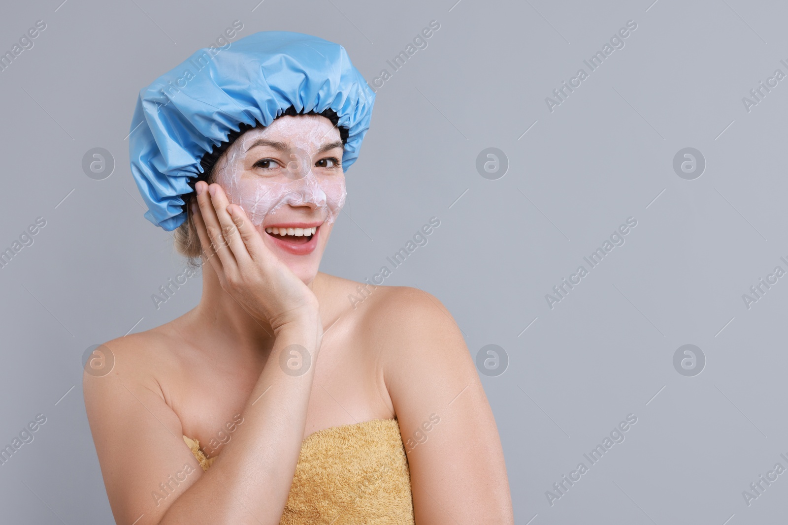 Photo of Woman with shower cap and cream on her face against grey background, space for text