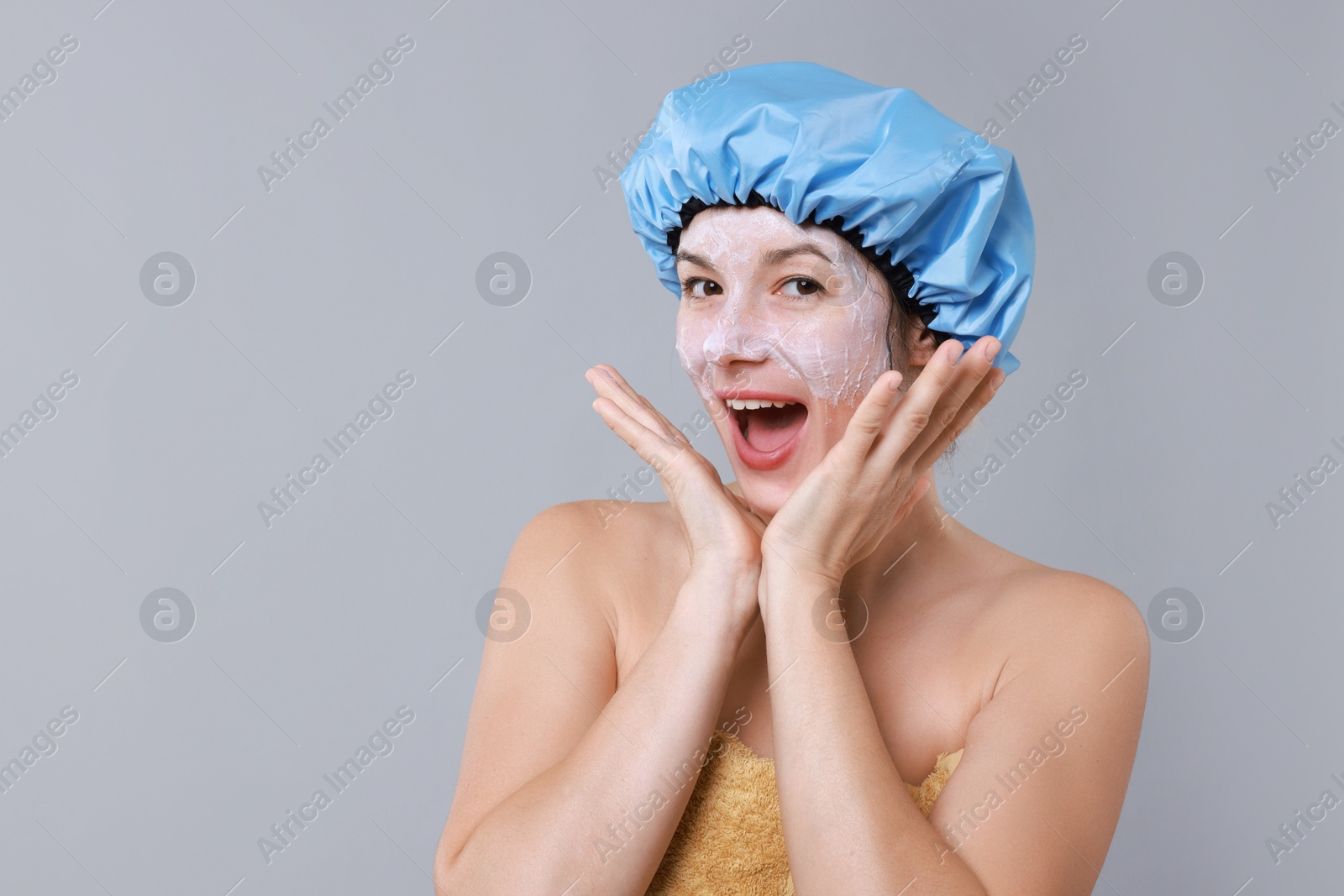 Photo of Woman with shower cap and cream on her face against grey background, space for text