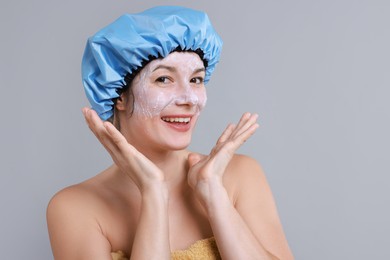 Photo of Woman with shower cap and cream on her face against grey background