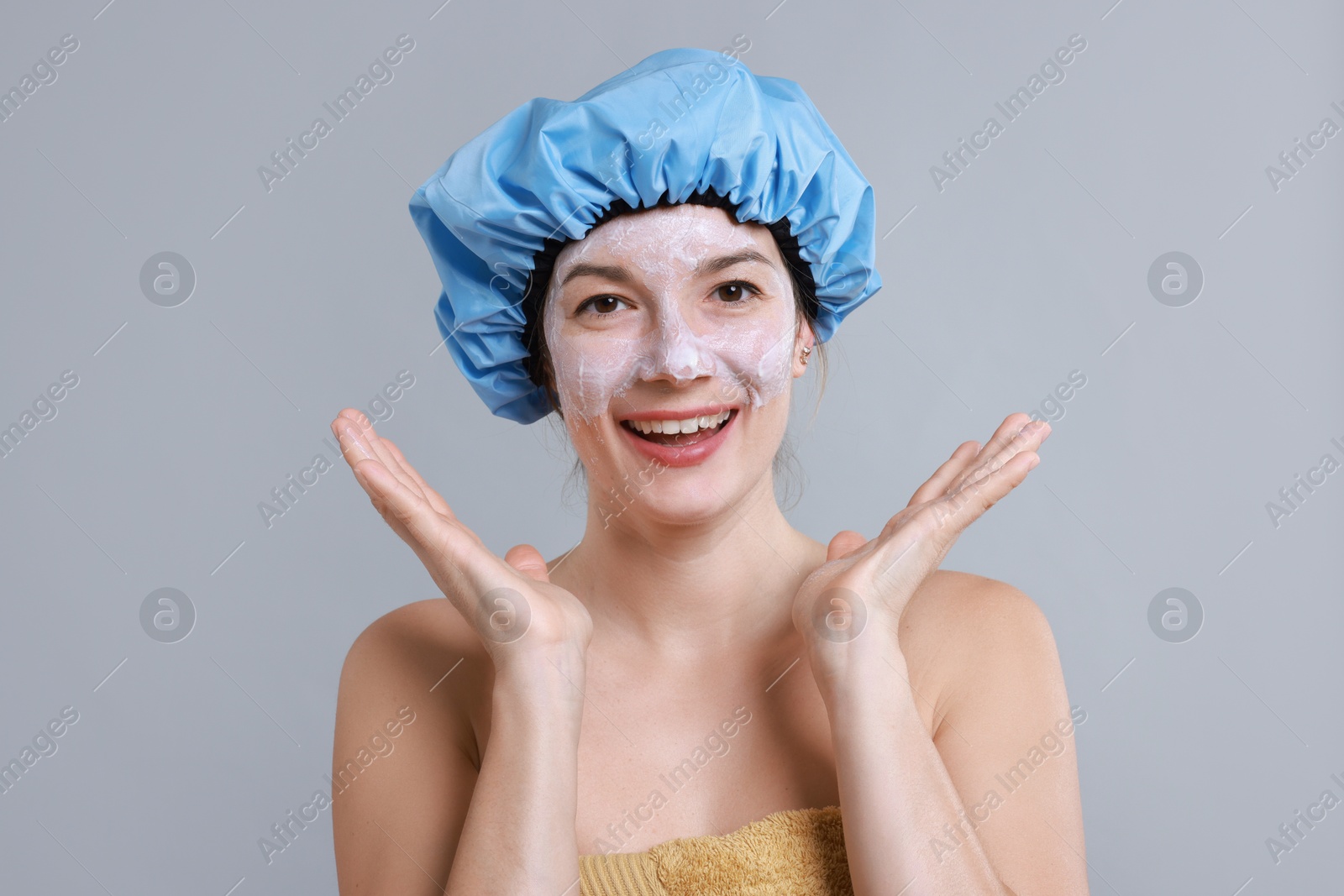 Photo of Woman with shower cap and cream on her face against grey background