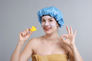 Photo of Woman with shower cap and bath duck showing ok gesture on grey background