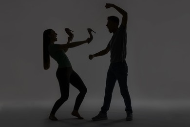 Photo of Domestic violence. Silhouette of man threatening his wife on grey background