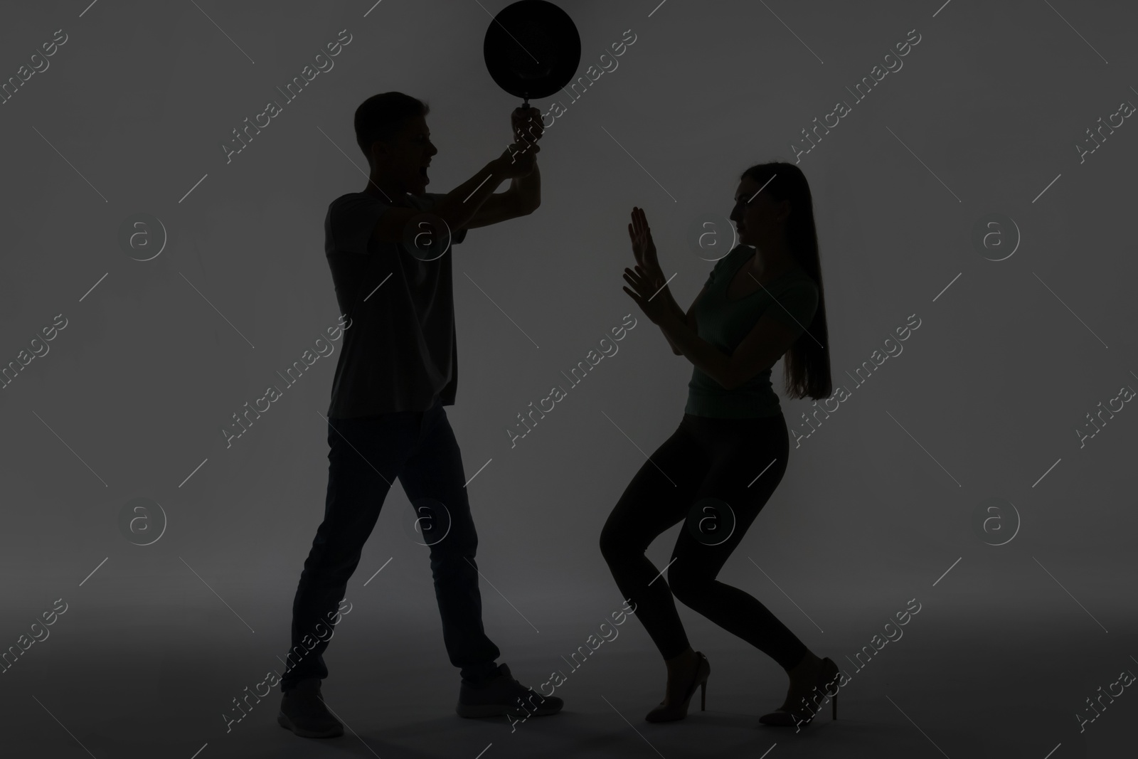 Photo of Domestic violence. Silhouette of man with frying pan threatening his wife on grey background