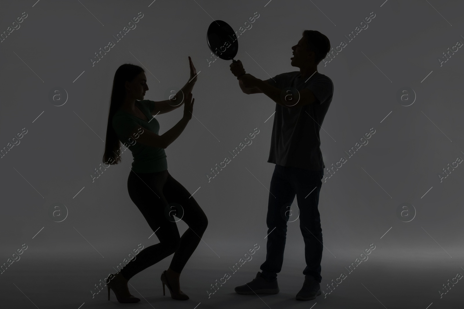 Photo of Domestic violence. Silhouette of man with frying pan threatening his wife on grey background