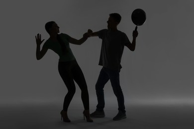 Domestic violence. Silhouette of man with frying pan threatening his wife on grey background