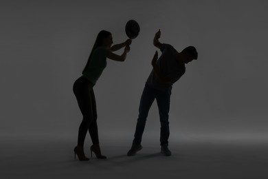 Photo of Domestic violence. Silhouette of woman with frying pan threatening her husband on grey background