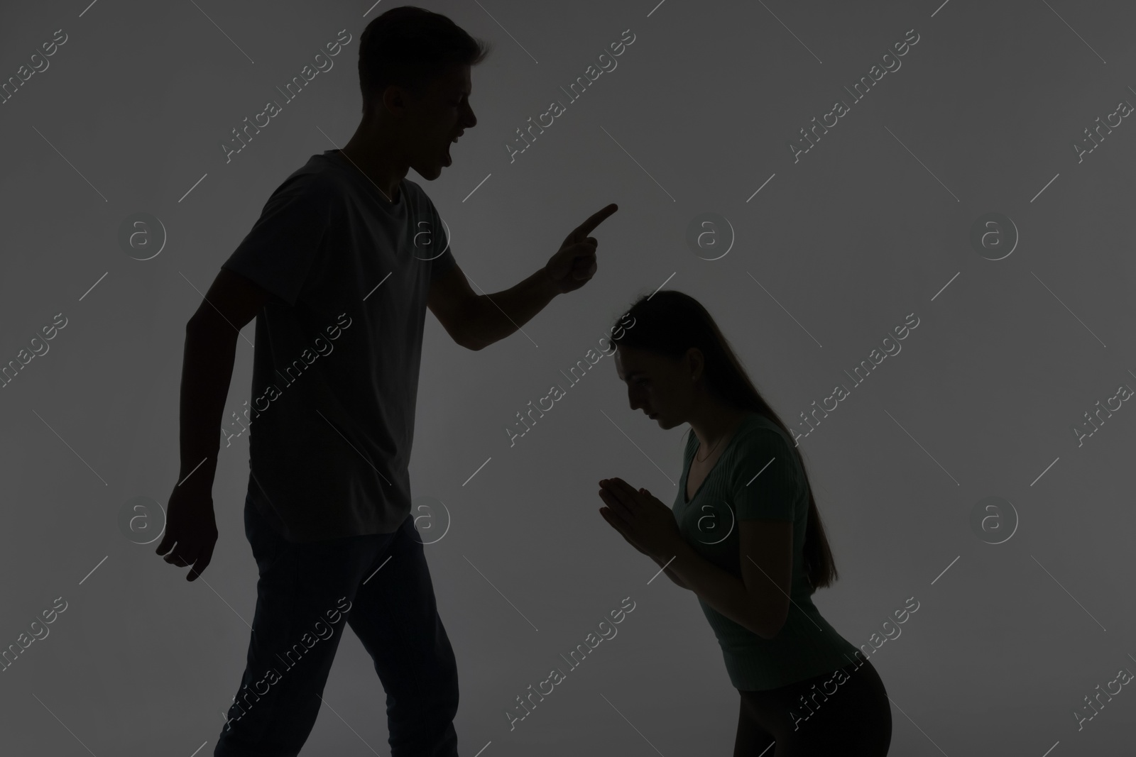 Photo of Domestic violence. Silhouette of man threatening his wife on grey background