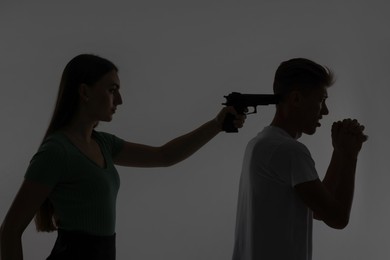 Photo of Domestic violence. Silhouette of woman with gun threatening her husband on grey background