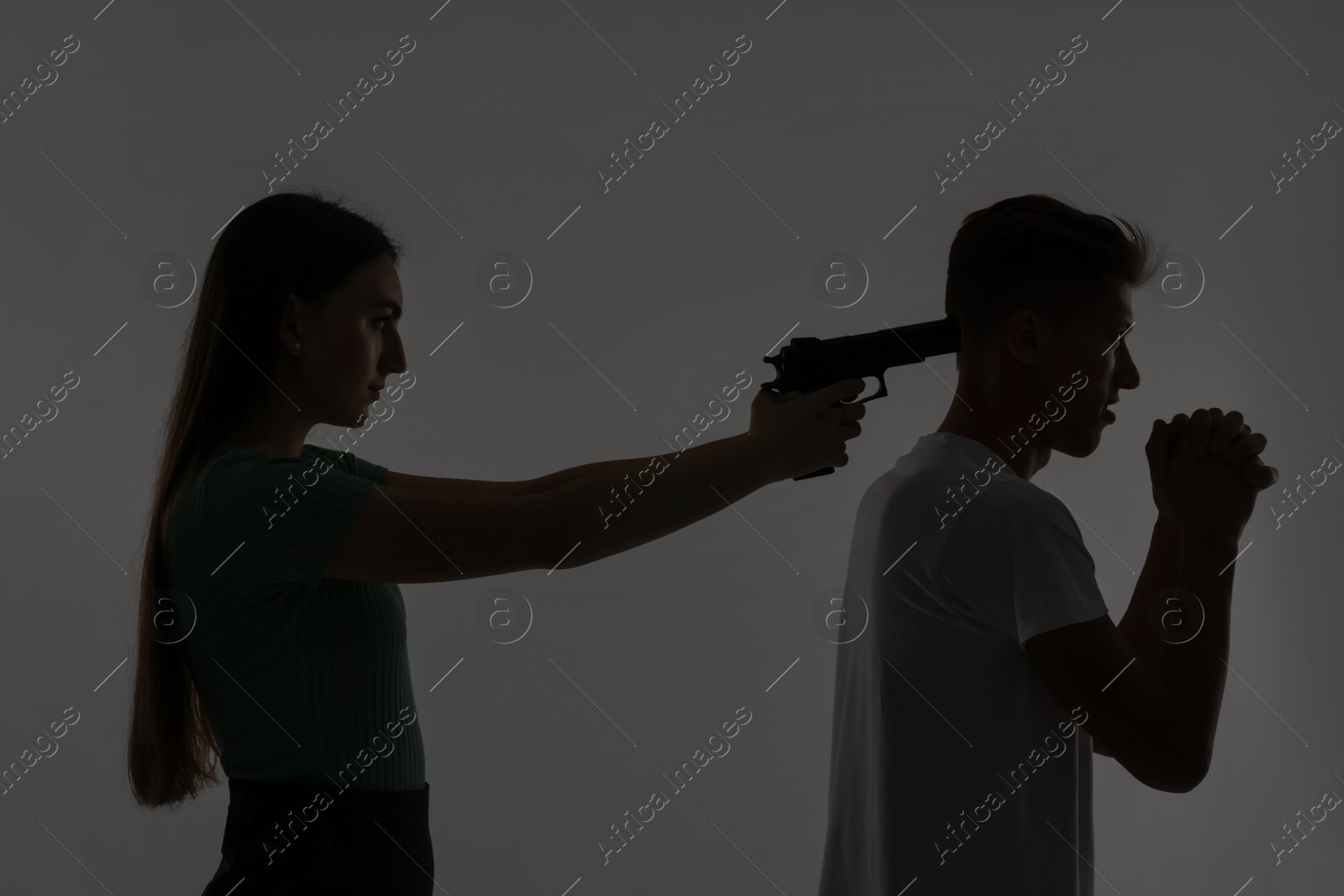 Photo of Domestic violence. Silhouette of woman with gun threatening her husband on grey background