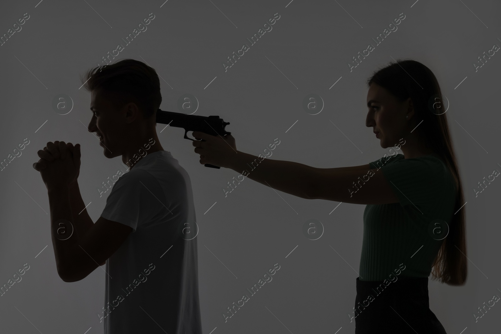 Photo of Domestic violence. Silhouette of woman with gun threatening her husband on grey background