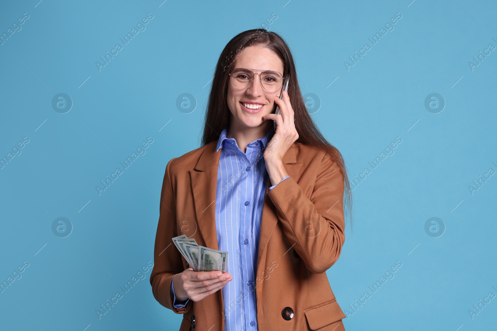 Photo of Banker with dollar banknotes talking on smartphone against light blue background