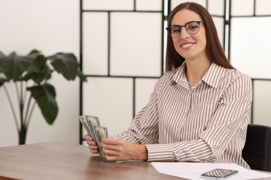 Photo of Banker with dollar banknotes at wooden table in office. Space for text