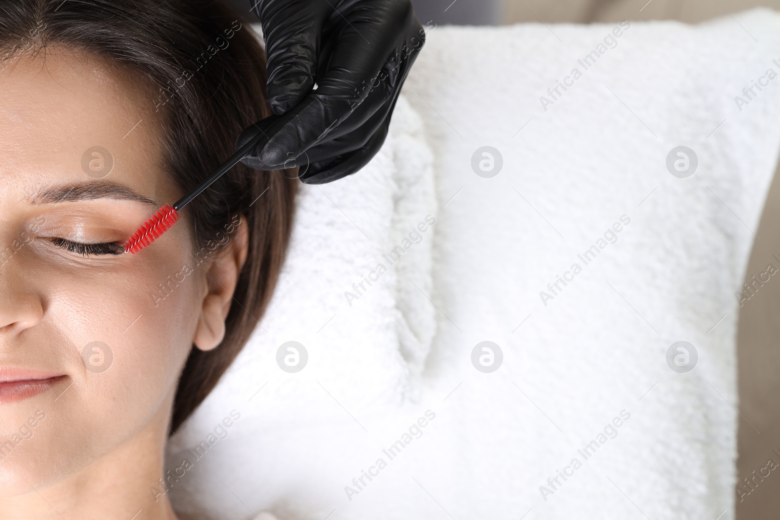 Photo of Eyelash extension procedure. Esthetician combing woman's lashes with brush in beauty salon, closeup. Space for text