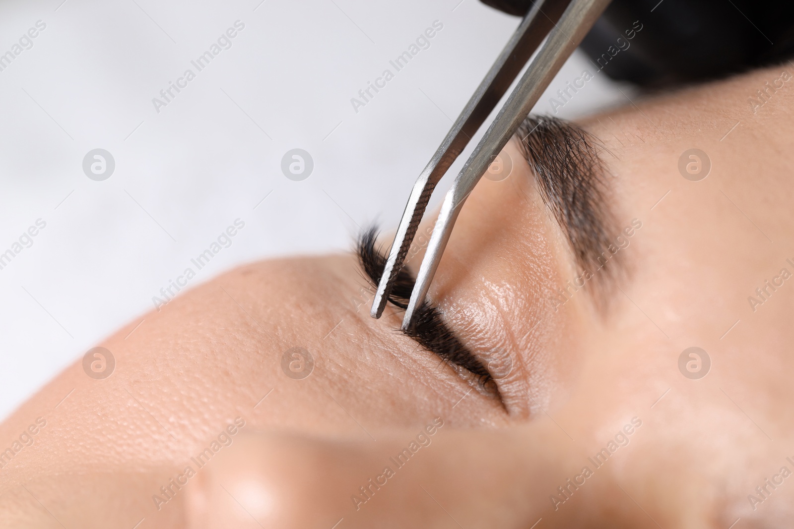 Photo of Woman undergoing lash extensions procedure in beauty salon, closeup