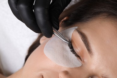 Photo of Woman undergoing lash extensions procedure in beauty salon, closeup