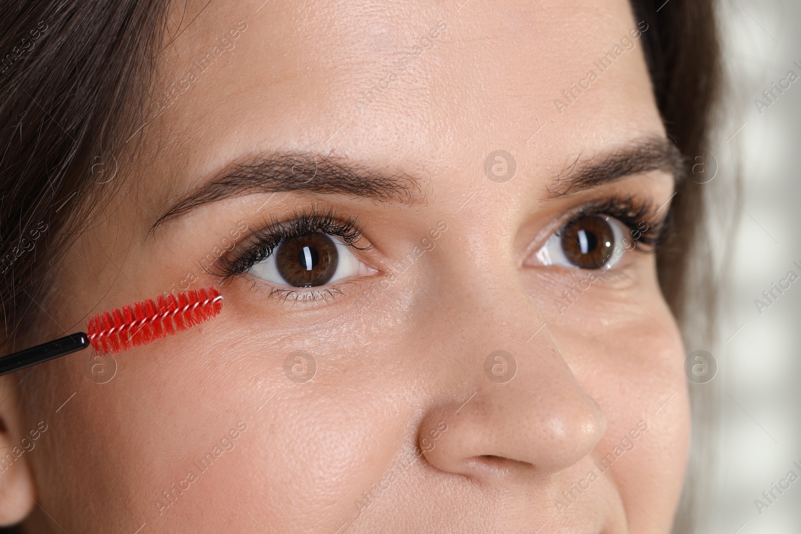 Photo of Eyelash extension procedure. Woman combing lashes with brush, closeup