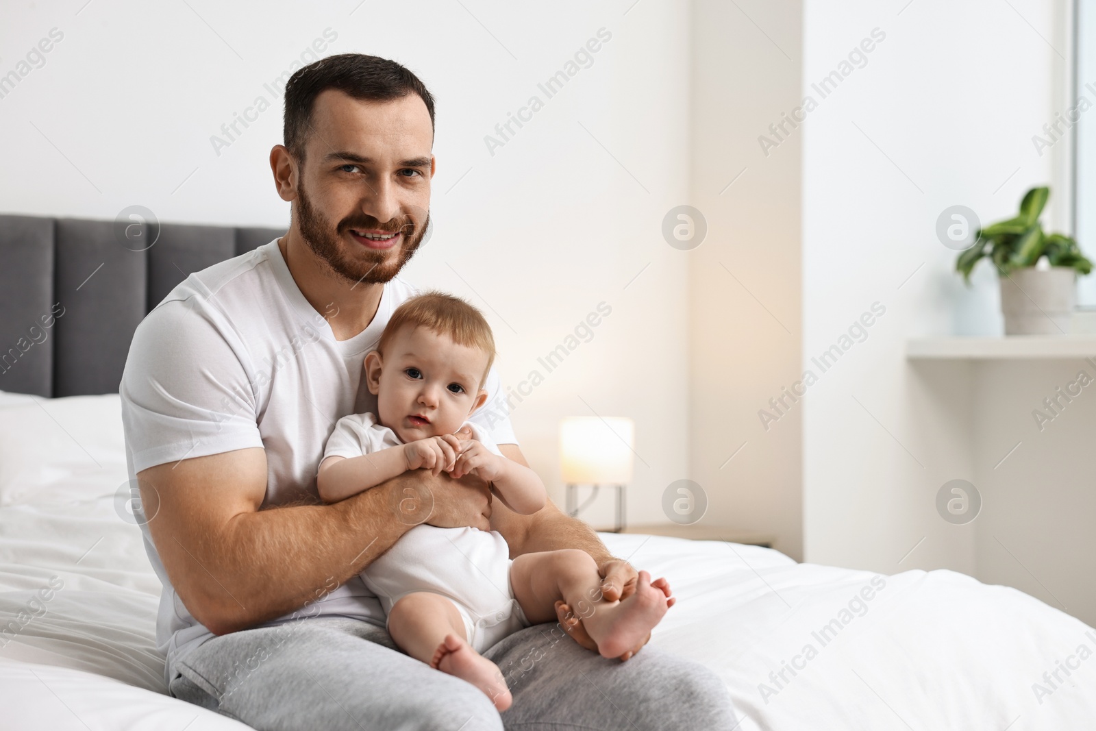 Photo of Father with his little baby on bed at home. Space for text