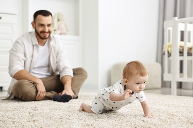 Photo of Father watching his little baby learning to crawl at home, selective focus