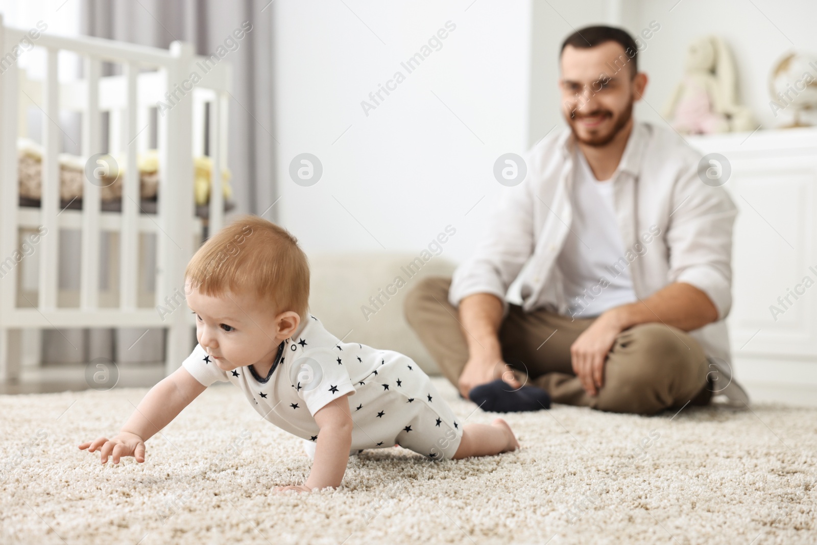 Photo of Father watching his little baby learning to crawl at home, selective focus