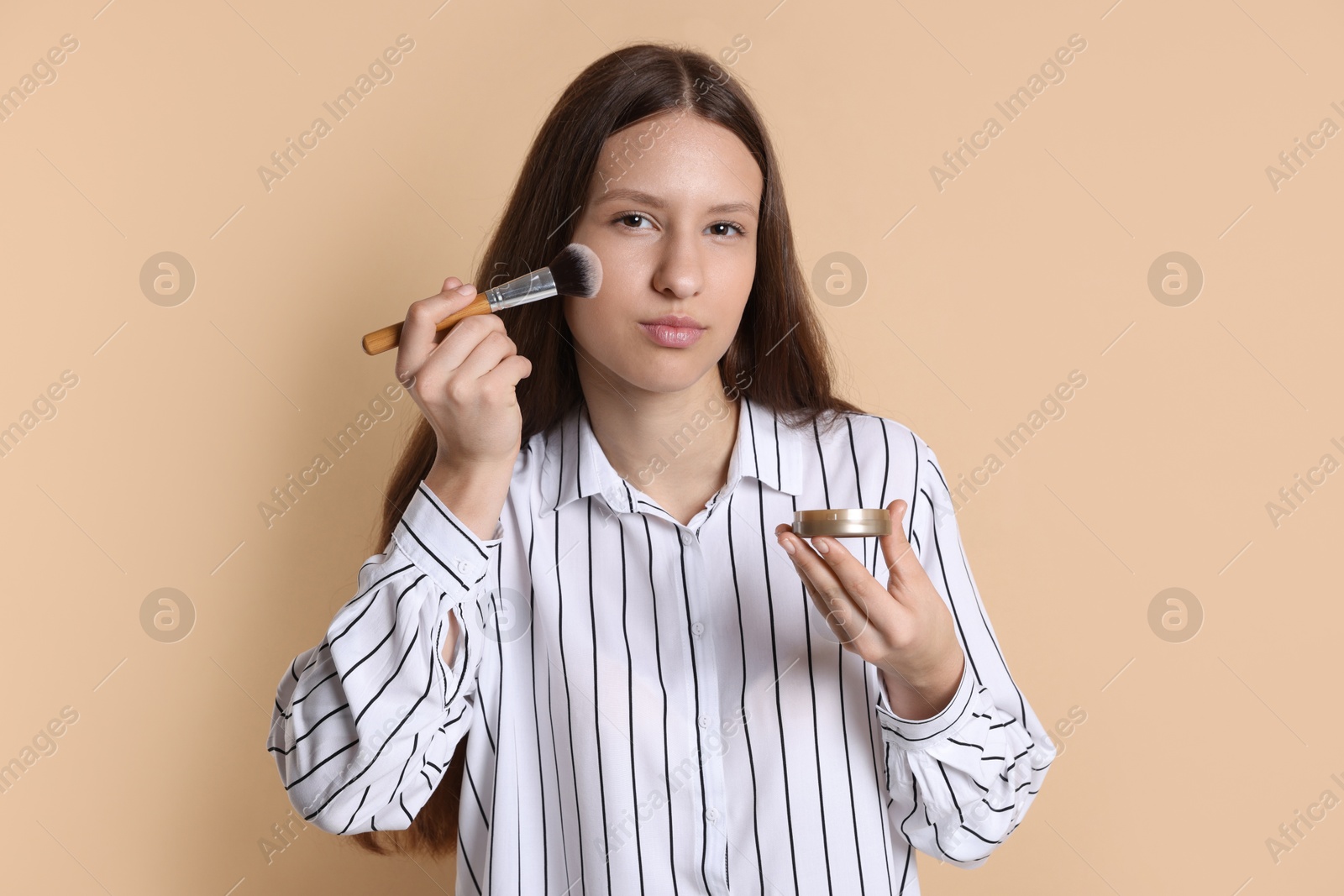 Photo of Teenage girl applying blusher on beige background