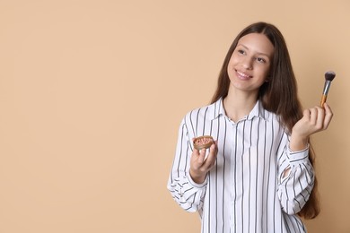 Photo of Smiling teenage girl with blusher and makeup brush on beige background. Space for text