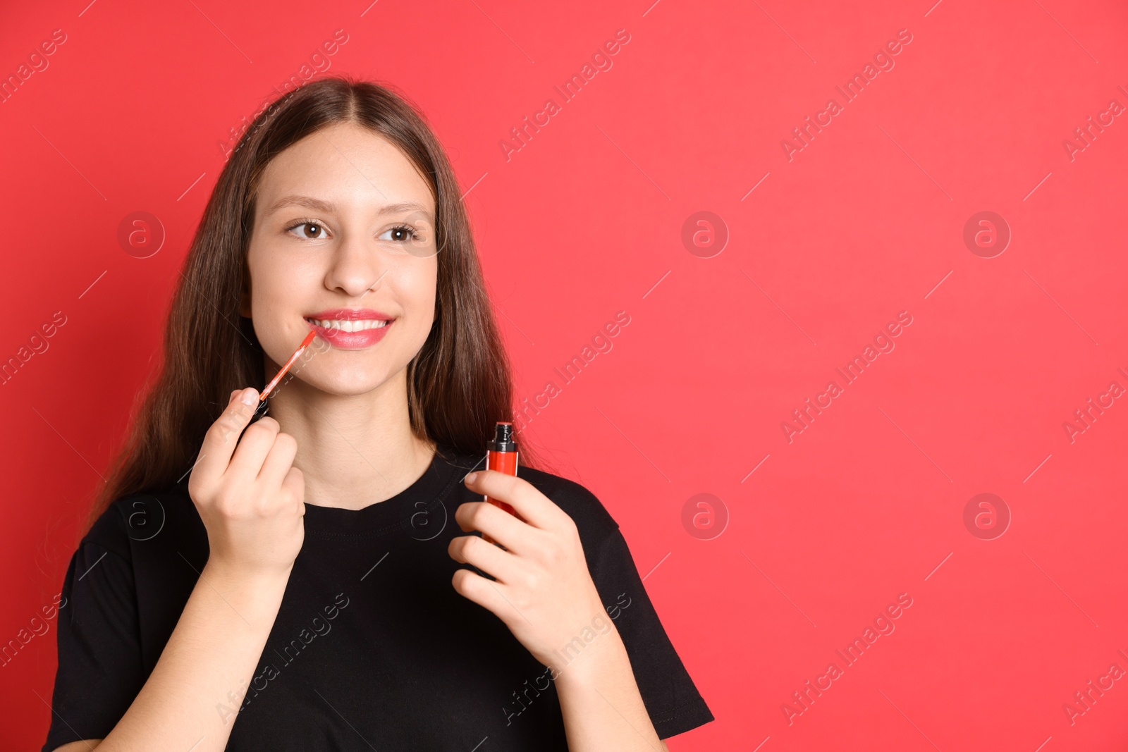 Photo of Smiling teenage girl applying lip gloss on red background. Space for text