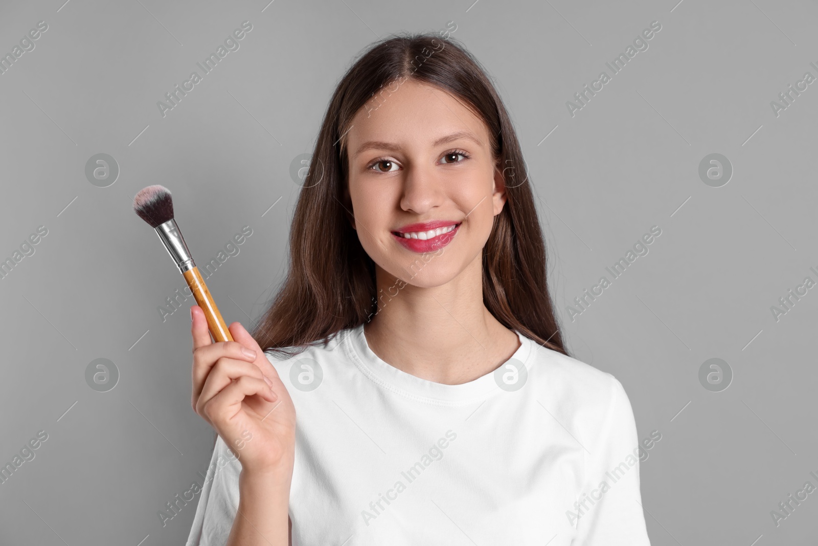 Photo of Smiling teenage girl with makeup brush on grey background