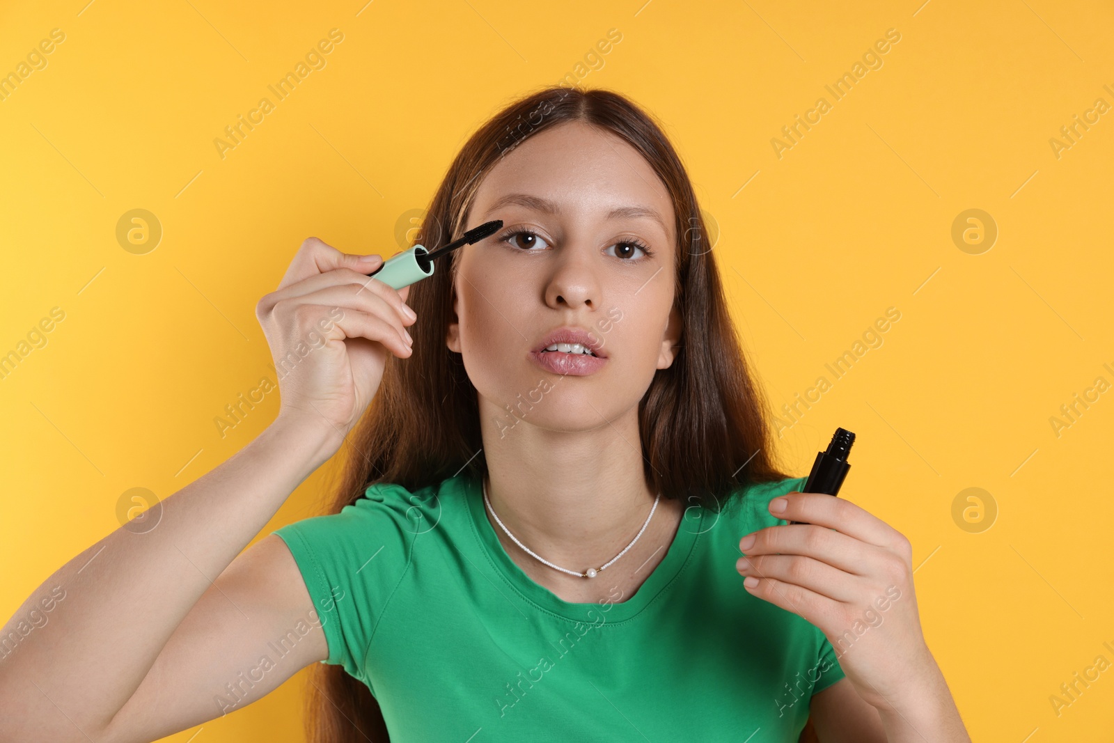 Photo of Teenage girl applying mascara on yellow background