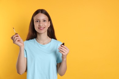 Photo of Smiling teenage girl with lip gloss on yellow background. Space for text