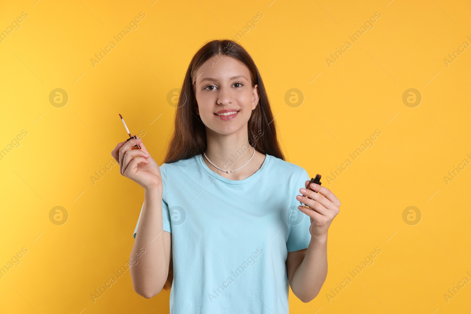 Photo of Smiling teenage girl with lip gloss on yellow background