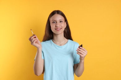 Photo of Smiling teenage girl with lip gloss on yellow background