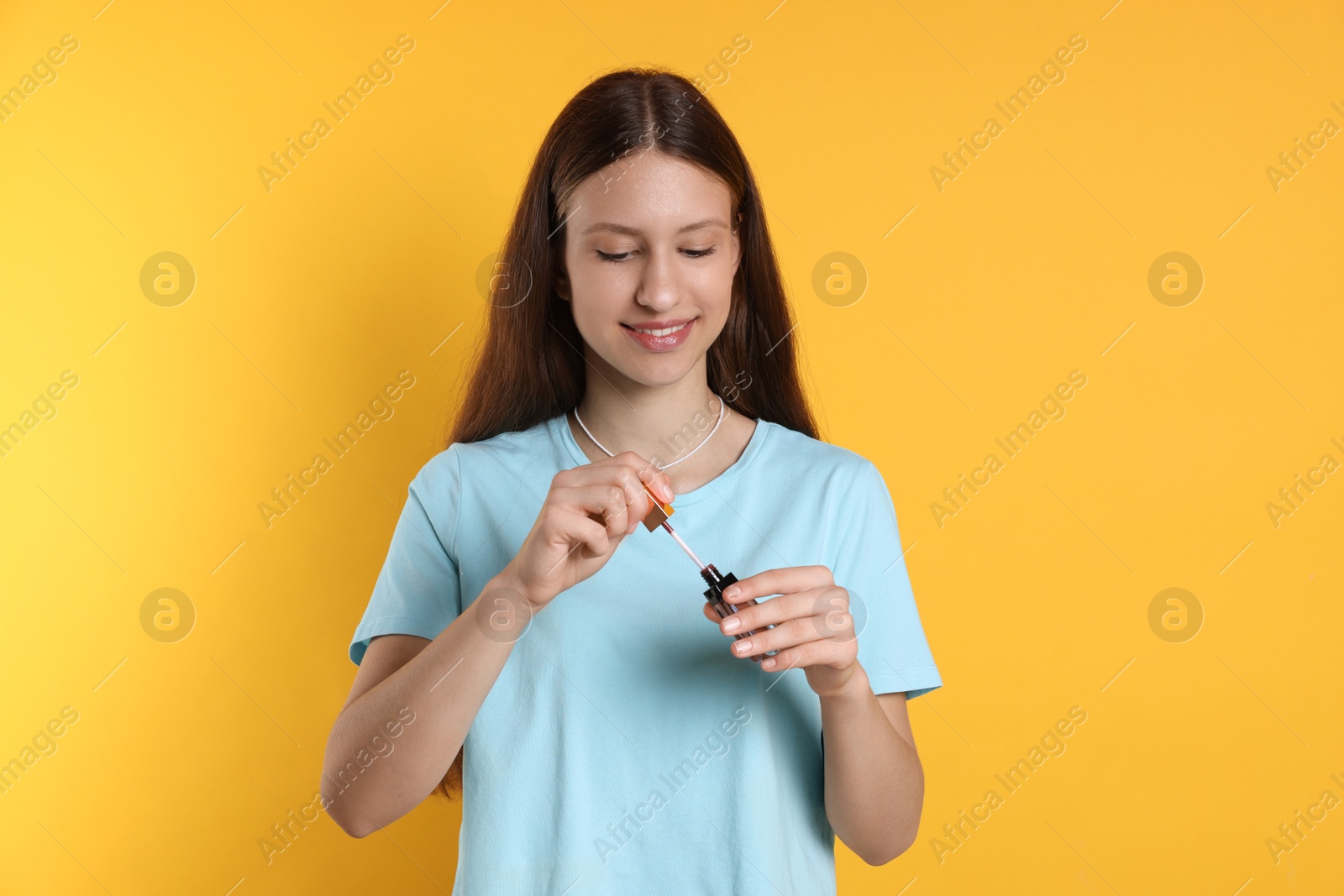 Photo of Smiling teenage girl with lip gloss on yellow background