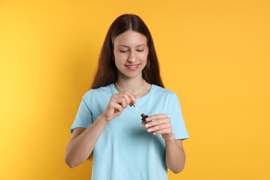 Photo of Smiling teenage girl with lip gloss on yellow background